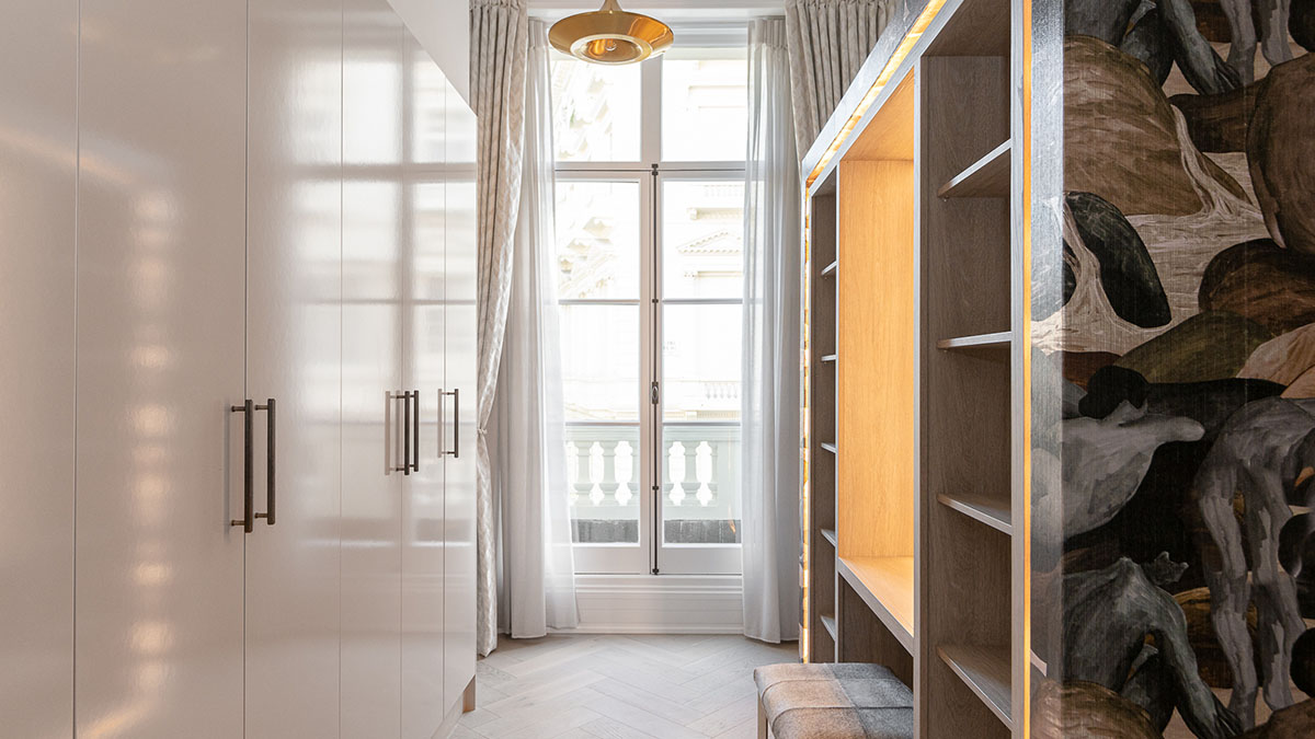 Elegant London Flat Dressing Room Design Elegant dressing room in a London flat, showcasing a full-height white wardrobe, built-in shelving, and a large window