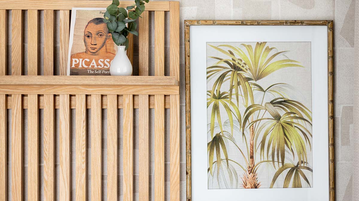 A close-up of a stylishly decorated London flat bedroom with a wooden headboard, art print, and a Picasso book