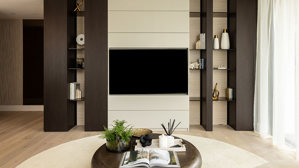 Modern living room with built-in TV wall unit, dark wood shelving, decorative accessories, and minimalist styling