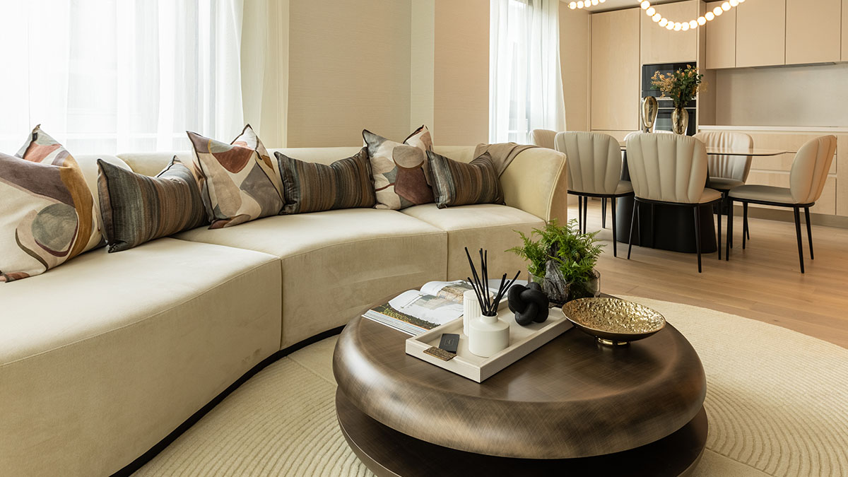 Modern open-plan living and dining area with curved beige sofa, wooden coffee table, and neutral-toned contemporary kitchen