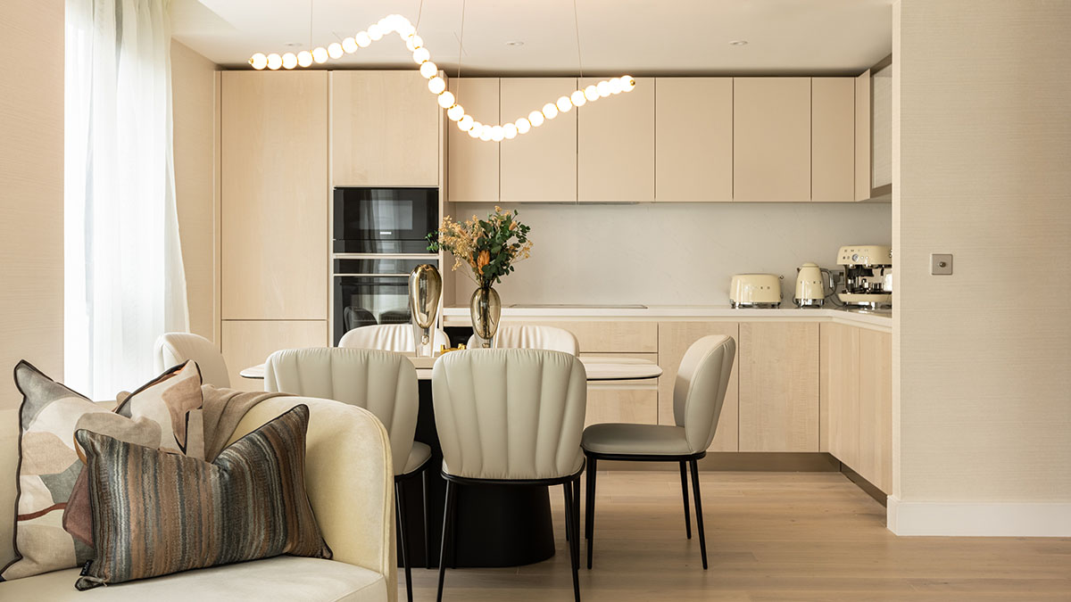 Modern open-plan kitchen and dining area with beige cabinetry, upholstered chairs, and contemporary pendant lighting